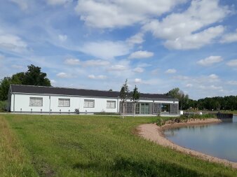 länglicher Flachbau mit weißer Außenfassade am Teich 