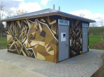 Quadratischer Flachbau mit Schrägdach aus Metall, Eingangstüren aus Edelstahl und Graffiti in Erdtönen an Fassade