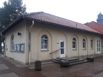 Flachbau mit Walmdach aus Ziegeln und gelber Fassade.Drei Stufen mit Handlauf vor weißer Eingangstür. 