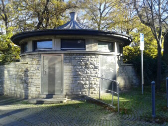 kreisförmiger Baukörper aus Natursteinmauerwerk mit Oberlichtern und Edelstahltüren 