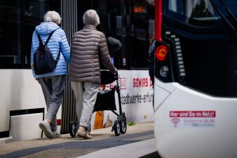 zwei ältere Frauen, davon eine mit Rollator, gehen an einer Haltestelle zwischen zwei Straßenbahnen 