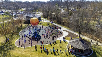 Ein Spielpark in der Natur mit Klettergerüsten und Pavillon, viele Familien mit Kindern spielen. Daufsicht von obe 