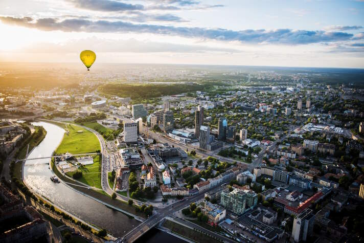 Ein gelber Heißluftballon fliegt über die Skyline der Stadt Vilnius in der Abendsonne