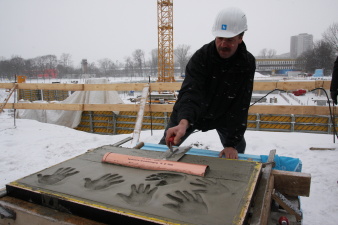 Ein Bauarbeiter streicht mit der Maurerkelle den Beton des Grundsteins glatt.
