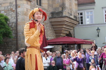 Vor dem Rathaus haben sich viele Menschen um Till Eulenspiegel versammelt.