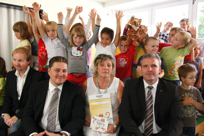 Foto: TigerKids © Stadtverwaltung Erfurt Vorn im Bild sitzen Oberbürgermeister Andreas Bausewein, die Leiterin des Kindergartens Matienkäfer, der designierte Thüringer AOK-Landesgeschäftsführer Matthias Dusel und ein weiterer Mann (v.r.n.l.); dahinter steht eine Gruppe jubelnder Kinder.