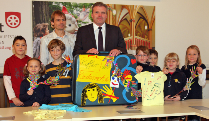 Der Oberbürgermeister und sieben Kinder mit dem bunt dekorierten Koffer.