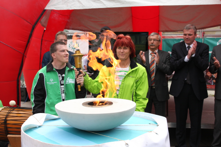 Foto: Olympisches Feuer © Stadtverwaltung Erfurt Zwei "Olympics"halten die brennende Fackel. Hinter ihnen stehen Vertreter aus Sport und Politik.