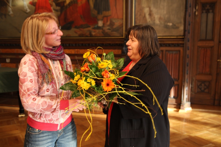 Eine Neubürgerin erhält von der Bürgermeisterin einen Blumenstrauß.