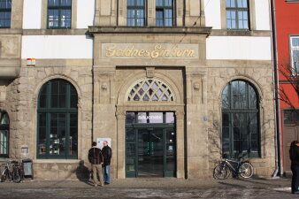 Zugang zu einem Haus mit grünen Fenstern und grüner Tür. Auf der Fassade steht "Goldnes Einhorn". 