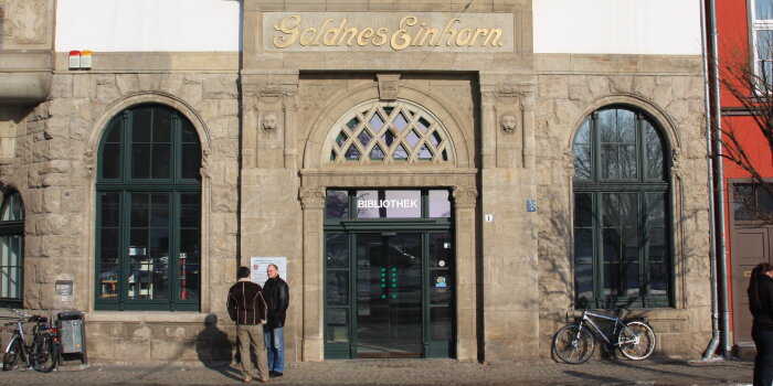 Zugang zu einem Haus mit grünen Fenstern und grüner Tür. Auf der Fassade steht "Goldnes Einhorn". 