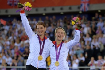 Zwei Sportlerinnen freuen sich und winken mit Blumen