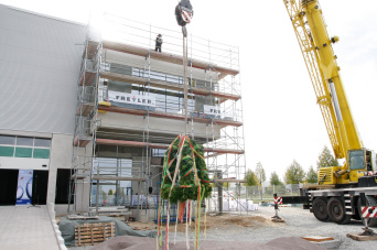 Der Richtkranz schwebt am Autokran vor dem eingerüsteten Rohbau.