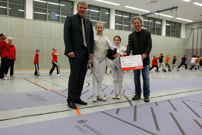 Zwei junge Fechterinnen erhalten den symbolischen Spendenscheck für die neue Fechtbahnen