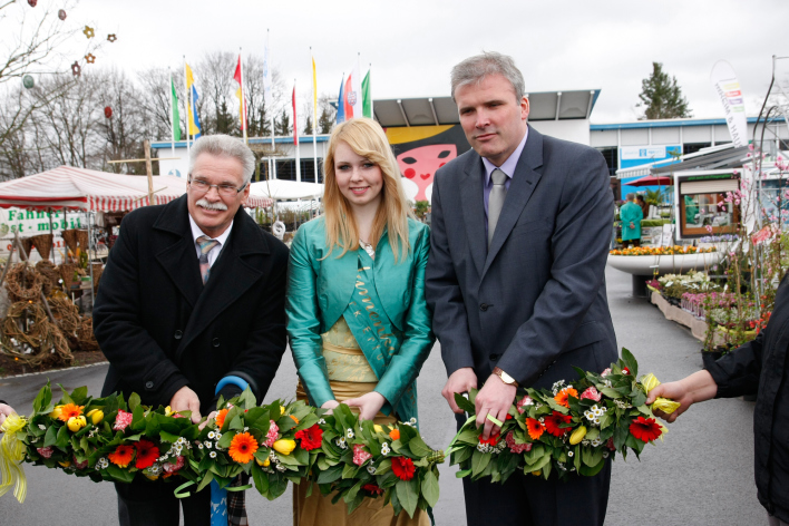 Ein Herr des Aufsichtsrates, Oberbürgermeister und Blumenkönigin durchschneiden eine Girlande