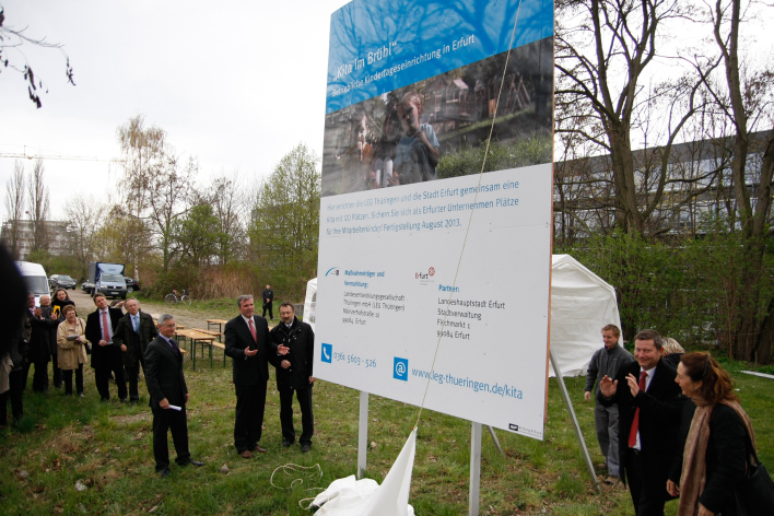 Oberbürgermeister, Bauherr und Bauleute vor einem großen Bauschild