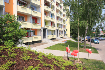 Frische Farben auf einer Wohnhausfassade, davor Sitzgelegenheiten im Grünen.