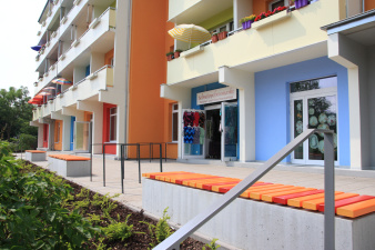 Frische Farben auf einer Wohnhausfassade, davor Sitzgelegenheiten im Grünen.