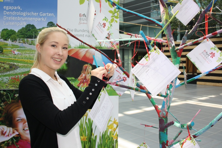 Foto: Wunschbaum für die Bundesgartenschau 2021 © Stadtwerke Erfurt Eine junge Frau hängt einen Wunschzettel an den Wunschbaum für die Bundesgartenschau 2021 im Atrium der Stadtwerke Erfurt.