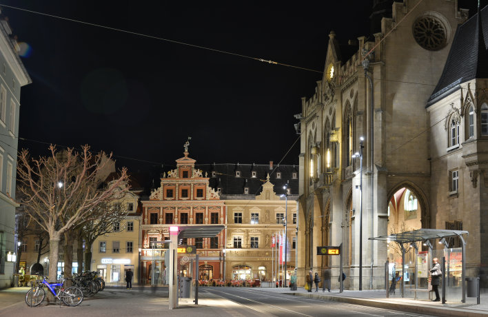 Nächtlicher Blick auf das Rathaus in Erfurt mit beleuchteter Fassade, davor eine barrierefrei gestaltete Straßenbahnhaltestelle.