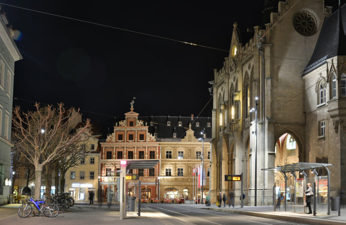 Foto: Umgestalteter Fischmarkt © Ingenieurbüro ITS, Gotha Nächtlicher Blick auf das Rathaus in Erfurt mit beleuchteter Fassade, davor eine barrierefrei gestaltete Straßenbahnhaltestelle.