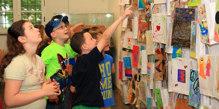 Eine Gruppe von Kindern bestaunt eine Wand voller bunt gestalteter Papiertüten.