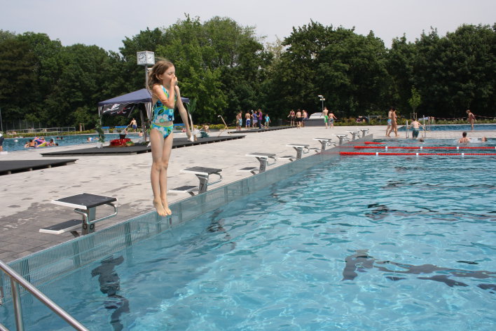 Ein Mädchen springt vom Startblock ins Schwimmbecken.