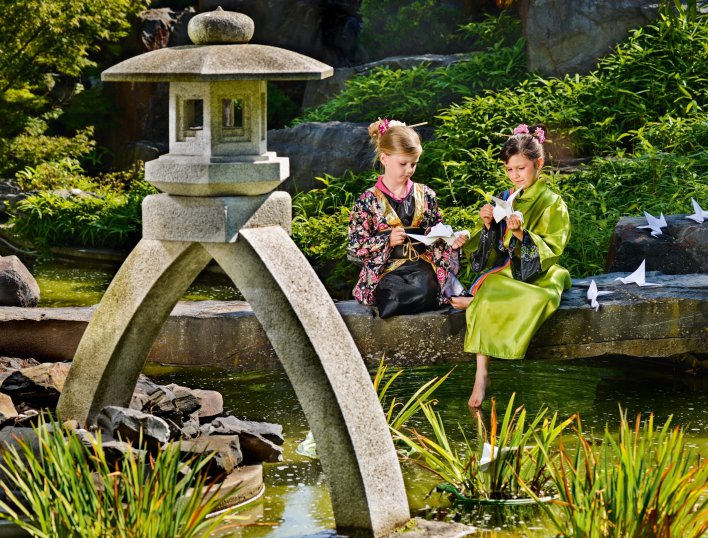 Zwei Mädchen in japanischer Kleidung im japanischen Garten die Papierkraniche falten. 