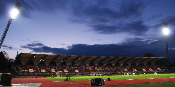 Vom Flutlicht hell erleuchtetes Stadion vor blauer Abenddämmerung.