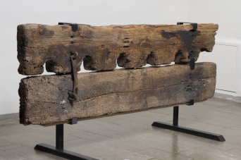 Ein hölzerner Pranger aus dem 13. Jahrhundert aus zwei schweren, übereinander liegenden Holzbalken mit Metallbeschlägen. 