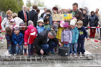 Eine Kindergruppe sowie zahlreiche Gäste beobachten den Oberbürgermeister der das Loch der Rohrhülse mit Mörtel verschließt. 