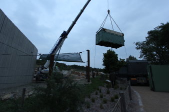 Ein Container hängt an einem Kran und wird über eine Mauer auf das Gelände der Elefantenanlage gehoben. 