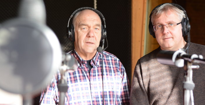 Zwei männliche Pesonen mit Kopfhörern hinter Mikrofonen