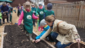 Foto: Schulgarten © Stadtwerke Erfurt Gruppe Eine Gruppe Kinder setzt Kartoffeln in einem Beet. Ein Mädchen in Gummistiefeln läuft das Beet ab, damit die Kartoffeln den richtigen Abstand zueinander haben - nach jedem Schritt eine Kartoffel.