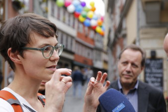 Eine junge Frau mit kurzen dunklen Haaren und Brille, die Künstlerin, erklärt eine im Hintergrund zu sehende Installation aus Luftballons zwischen den Häusern der Krämerbrücke. 