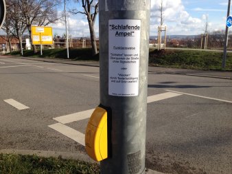 Pfosten einer Ampel, darauf der Hinweis: "Schlafende Ampel. Funktionsweise: Schlafen lassen und Überqueren der Straße ohne Signalschutz oder Wecken durch Tasterbetätigung und auf grün warten"