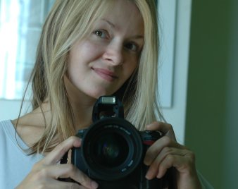 Portraitfoto der Künstlerin Beata Kotecka: eine junge, lächelnde, blondhaarige Frau mit einer Kamera in der Hand