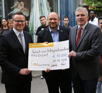 Drei männliche Personen präsentieren einen Scheck über 10.000 Euro.