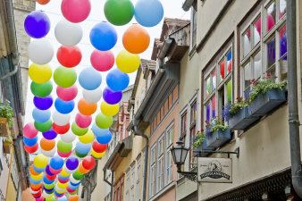Blick von unten nach oben, zwischen die Häuser der Krämerbrücke, zwischen denen hunderte bunte Luftballons aufgehängt sind. 