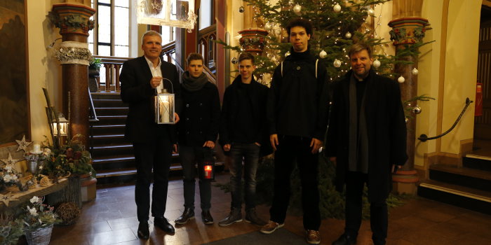 Oberbürgermeister Andreas Bausewein steht mit drei jungen Männern und einem Pfarrer im Foyer des Rathauses, er und einer der jungen Männer halten in der Hand jeweils eine Laterne mit dem Friedenslicht. 