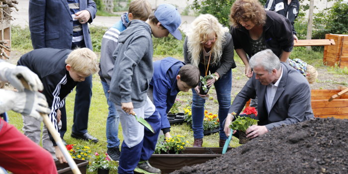 Oberbürgermeister Andreas Bausewein bepflanzt mit ein paar Kindern und Erwachsenen auf einer Rasenfläche einen Balkonkasten. 
