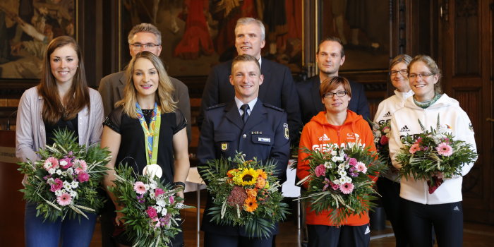 Sportlerinnen und Sportler stehen mit Blumen in der Hand in einem Saal.