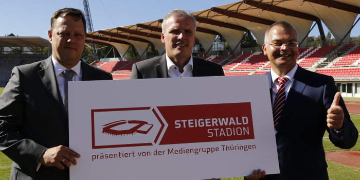 Drei Herren stehen im Innenraum des "Steigerwaldstadions" und halten gemeinam ein Schild mit dem Namenszug und Logo der Multifunktionsarena.