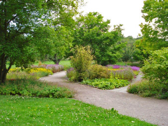 Durch einen Park schlängelt sich ein Kiesweg, rechts und links davon herrliche Begrünung durch Bäume, Büsche und Blumen.