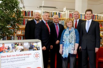 Sechs Personen stehen in der Bibliothek vor einem Bücherregel, links im Bild befindet sich ein Aufsteller mit einem Hinweis auf die neue Bildungsberatung. 