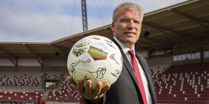 Ein Mann steht im Stadion und präsentiert einen Fußball.