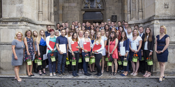 Foto: Gruppenbild der neuen Arbeitskräfte © Stadtverwaltung Erfurt Eine Gruppe von mehr als 50 Jugendlichen und jungen Erwachsenen steht auf schmalen Treppen aufgereiht zwischen und vor einem historischen Bauwerk, dem Rathaus der Stadt Erfurt.