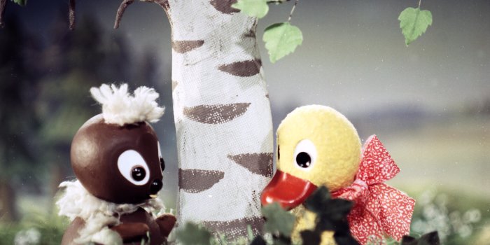 Die Figuren Pittiplatsch und Schnatterinchen aus dem Kinderfesnehprogramm sitzen im Gras.