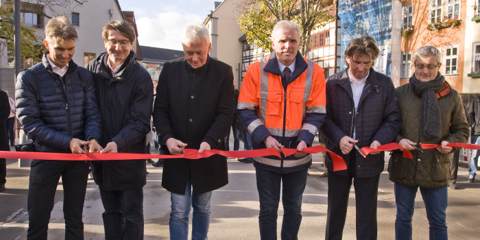 Sechs Männer stehen auf einer Brücke und schneiden ein rotes Band durch.