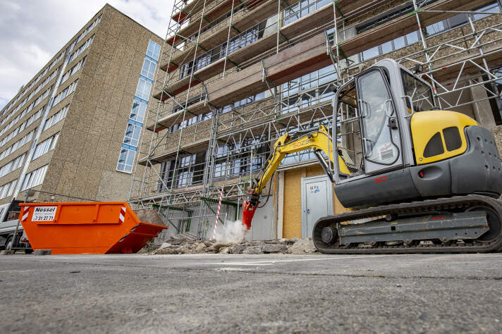 Ein Bagger steht vor dem eingerüsteten Gebäude